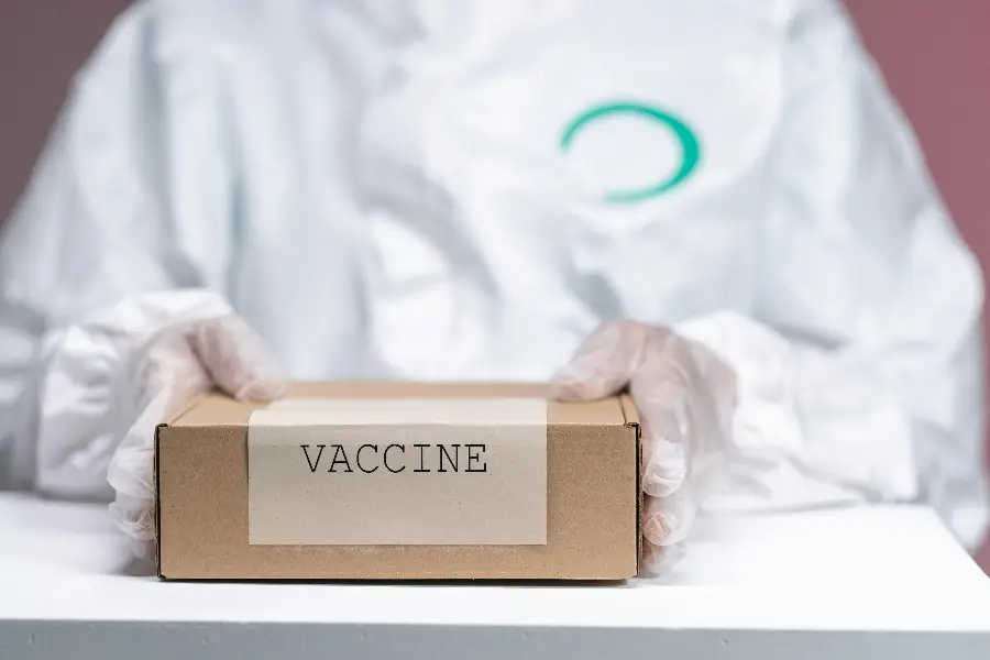 Healthcare worker holding a vaccine package in protective gear, emphasizing safety and health.